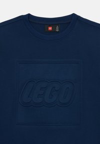 Camiseta de algodón azul marino con un logo de LEGO en relieve en el centro, mangas cortas y cuello redondo.