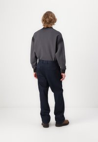 Gray sweatshirt with long sleeves and ribbed cuffs, paired with navy wide-leg trousers. Both items feature a relaxed fit. Brown boots complete the look.