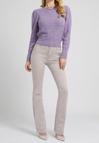 Lila gebreide trui met opgepofte mouwen en een geribde zoom, gecombineerd met licht beige nauwsluitende broek, beide met een gladde textuur.