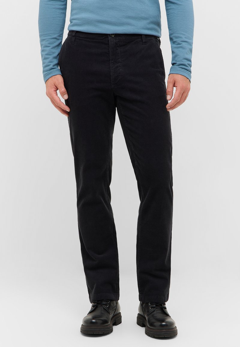 Czarne spodnie kordurowe o prostym kroju, z fakturowaną powierzchnią. W połączeniu z czarnymi butami za kostkę na sznurówki i niebieską koszulą z długim rękawem.