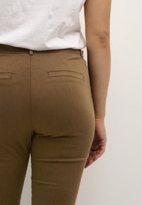 Brown tailored pants with a smooth texture, featuring two back pockets and a slim fit, paired with a white shirt.