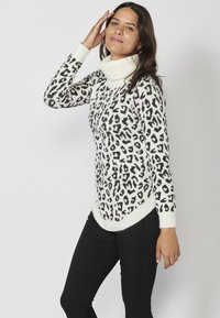 Stickad polotröja med ett svart och brunt leopardmönster på vit botten, med ribbade ärmslut och fåll. Långa ärmar, avslappnad passform.