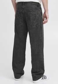 Jeans negros de mezclilla con un ajuste holgado, con un ligero desgaste, dos bolsillos traseros y una pretina sencilla, combinados con zapatillas blancas.