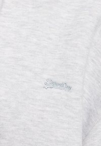 Helle graue Sweatshirt aus weichem Stoff mit subtiler Textur und einem blauen gestickten "SuperDry"-Logo auf der linken Seite.