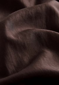 Tissu brun avec une texture lisse et légèrement brillante, présentant des plis et des ondulations subtils, créant une impression de profondeur et de dimension.