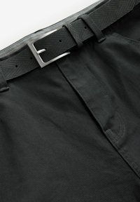 Pantaloni din țesătură neagră cu un finisaj texturat, care includ o curea neagră asortată cu un cataramă argintie. Au buzunare laterale și bucle pentru curea.
