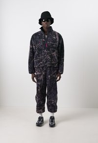 Fleece pullover and pants set in dark purple with abstract pattern, paired with a bucket hat, sunglasses, and black athletic shoes.