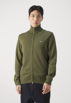 Olive green zip-up sweater with a high neck, knit texture, and a small logo detail on the chest. Features ribbed cuffs and hem.