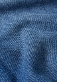 Denim fabric, medium blue hue, fine twill texture, slight sheen, slightly crumpled appearance, with visible stitching detail.