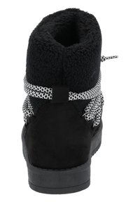 Botín de ante negro con un suave forro de lana negra, cordones trenzados en blanco y negro, y suela de goma negra plana.