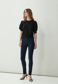 Maglione nero con maniche a sbuffo abbinato a pantaloni slim-fit blu navy. Il modello indossa sandali neri con tacco. Texture morbide, design semplice e senza motivi visibili.