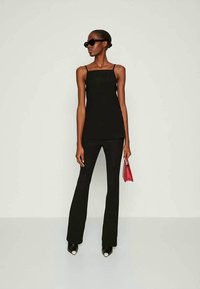 Črna brezrokavnica v kombinaciji s črnimi širokimi hlačami. Dodatki vključujejo majhno rdečo torbico in sončna očala. Material se zdi gladek, s prileganjem k telesu.