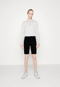 Světle šedé polo tričko se třemi knoflíky, doplněné černými džínovými šortkami. Model má na sobě světle šedé tenisky na jednobarevném pozadí.