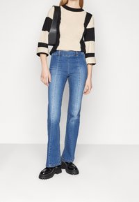 Suéter de punto con rayas negras y crema, combinado con unos pantalones de mezclilla acampanados en azul claro. Zapatos de plataforma negros y un bolso negro complementan el look.