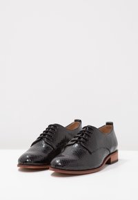Scarpe nere stringate con tomaia in pelle testurizzata a motivo rettile, punta arrotondata e tacco basso in legno marrone.