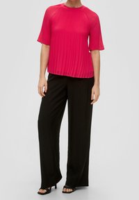 Blusa plisada rosa intenso de manga corta, combinada con pantalones de pierna ancha negros y tacones abiertos negros. Textura suave y ajuste relajado.