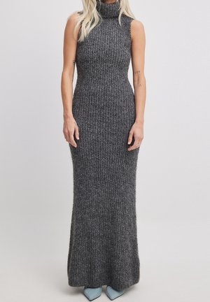 Femme portant une robe maxi sans manches en maille côtelée gris foncé avec un col roulé haut et des chaussures pointues bleu pâle.