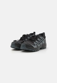 Chaussures d'extérieur noires avec tige texturée, accents gris, bandes réfléchissantes et semelle en caoutchouc robuste. Présentent des lacets ajustables pour un meilleur maintien.