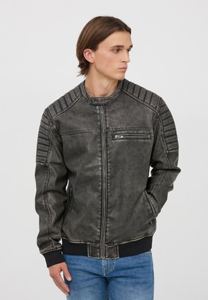 Giacca bomber in finta pelle grigia con dettagli a coste sulle spalle, tasca sul petto con zip e polsini in maglia. Indossata con jeans in denim blu.