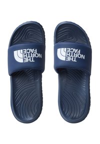 Sandalias de slide de color azul marino con una tira ancha que presenta el logo blanco "The North Face". Suela de goma texturizada con patrones en forma de ola para mayor grip.