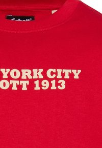 T-shirt in cotone rosso con scollatura a girocollo e testo in crema audace: "NEW YORK CITY 1913" stampato in modo prominente sul davanti.