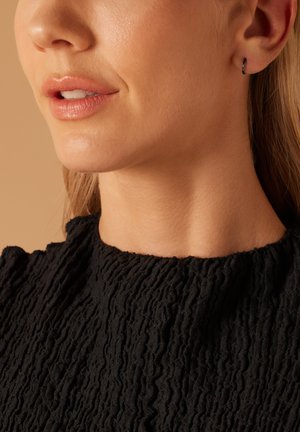 Zwart, textuurstof top met een ruches ontwerp. Close-up van een persoon zijn nek en gezicht met subtiele make-up en oorbellen.