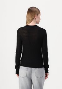 Svart ribbet strikket genser med lange ermer og rund hals. Har en kroppsnær fasong og lett transparent tekstur bak.