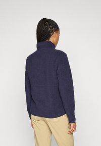 Navy blue fleece jacket with a high collar and textured, fluffy design. Features a relaxed fit and long sleeves. No visible hardware.