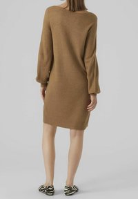 Robe pull en maille marron avec une coupe décontractée, des manches longues et un col en scoop. Texture lisse ; associée à des chaussures à rayures noires et blanches.