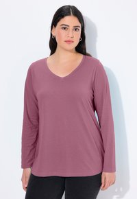 Košile s dlouhým rukávem a véčkovým výstřihem v tlumené růžové barvě s hladkým povrchem. Volný střih, ideálně se kombinuje s černými kalhotami.