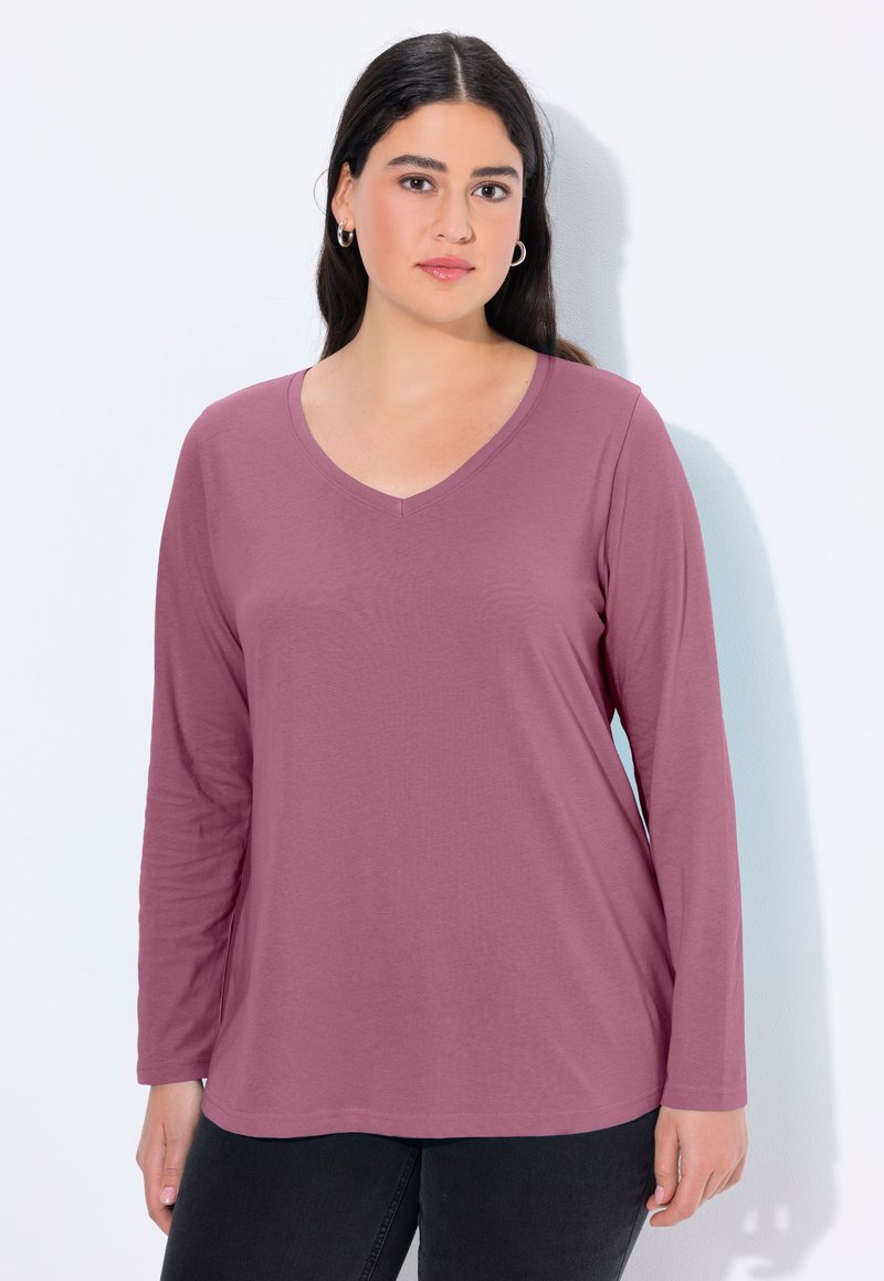 Košile s dlouhým rukávem a véčkovým výstřihem v tlumené růžové barvě s hladkým povrchem. Volný střih, ideálně se kombinuje s černými kalhotami.