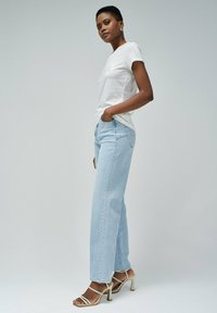 Camiseta blanca ajustada, jeans rectos de mezclilla azul claro y sandalias de tacón alto beige con tiras. Tejido texturizado con diseño clásico de mezclilla.