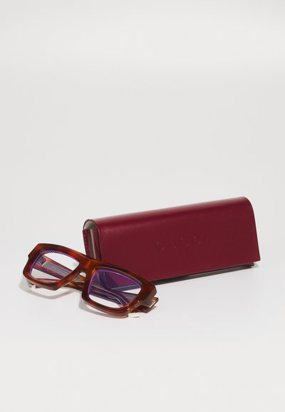 Gafas Gucci con un marco geométrico, grueso y de carey marrón. Las lentes están tintadas de púrpura. Acompañadas de un estuche rígido burdeos con logotipo en relieve.