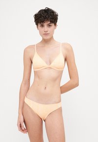 Trójkątny biustonosz bikini i pasujące majtki w delikatnym pastelowym pomarańczowym kolorze z subtelnymi wzorami geometrycznymi. Wykonane z gładkiego, elastycznego materiału.