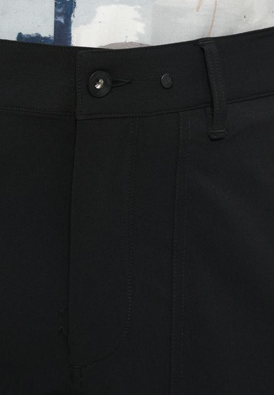 Pantalones negros con una textura suave, que presentan un cierre frontal con botón, lazos para cinturón y acentos de costura visibles.