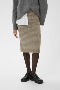 Falda a la altura de la rodilla con estampado de pata de gallo en tela marrón y negra, combinada con un suéter gris y zapatos negros, usada sobre medias negras transparentes.