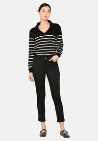 Polo de manga larga a rayas blancas y negras combinado con pantalones negros ajustados que tienen cremalleras en los tobillos y zapatos negros planos.
