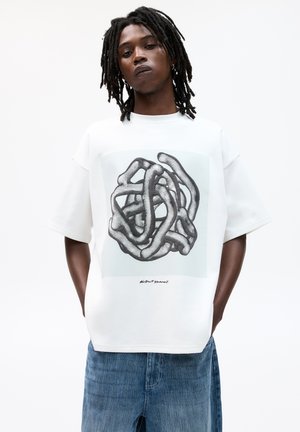 Hvid oversized t-shirt med et grafik af sammenflettede linjer i grå nuancer, med teksten "abstrakt øjeblik" nedenfor designet. Denim shorts.