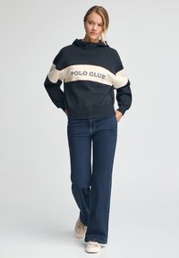 Marinblå och krämfärgad färgblockerad huvtröja med "POLO CLUB" broderat i mörka bokstäver, i kombination med vida jeans och ljusa sneakers.