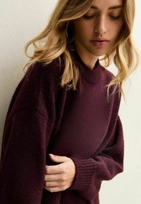 Maglione bordeaux realizzato in un morbido materiale testurizzato, con scollo rotondo a coste e maniche ampie, caratterizzato da dettagli sottili sui polsini.