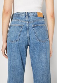 Hellblau gefärbte Jeans mit hoher Taille, geradem Bein und zwei hinteren Taschen. Braunes Lederlogo am Bund.
