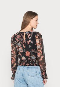 Blusa floral preta com flores coloridas. Manga longa transparente, cintura franzida e detalhe em forma de buraco na parte de trás. Combinada com jeans azul claro.