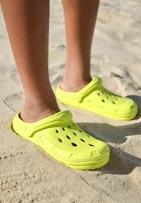 Élénk sárga klumpák, szellőzőlyukakkal, könnyű anyagból készültek, lekerekített orral és vastag, texturált talppal rendelkeznek.