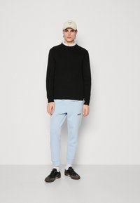 Black sweater, light blue sweatpants with "BOSS" logo, black sneakers, and a beige cap. Simple design, casual fit, with contrasting colors.