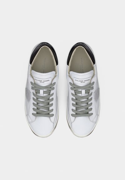 Paire de baskets basses blanches avec lacets gris, accents noirs au talon et étiquette "Philippe Model Junior" sur la languette, vue de dessus.