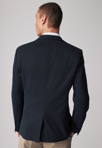 Blazer azul marino con un corte ajustado, una abertura en la parte posterior y cierre de dos botones. La tela se presenta suave con un ligero brillo.