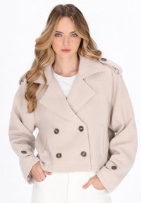 Beige cropped dobbelbrystet jakke med store mørke knapper, klippede lapeller og skulderepaulettes, lavet af et blødt, tekstureret stof.