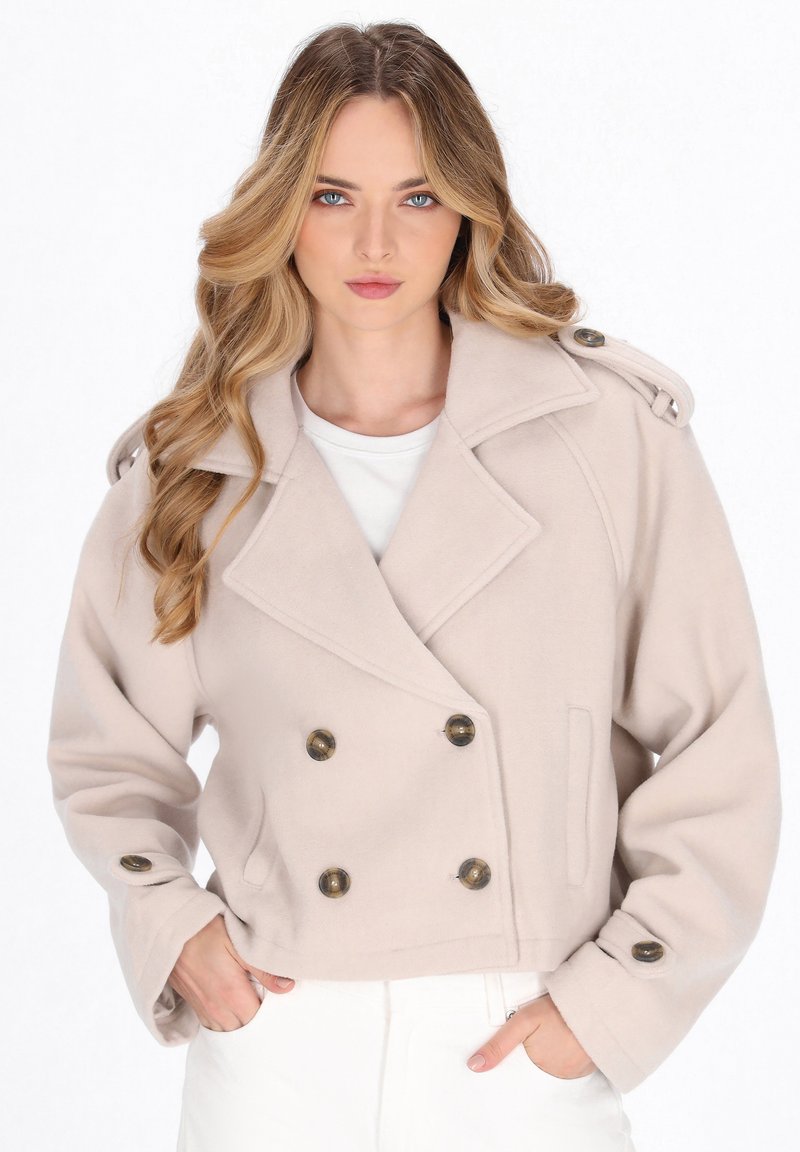 Beige cropped dobbelbrystet jakke med store mørke knapper, klippede lapeller og skulderepaulettes, lavet af et blødt, tekstureret stof.