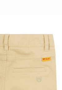 Khaki Baumwollhose mit glatter Textur, einer Gesäßtasche und einem gestickten Teddybär-Logo. Mit einem leuchtend gelben Markenetikett.