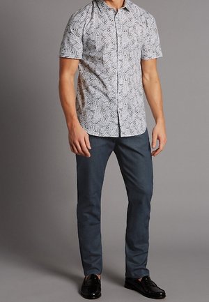 Korte mouwen overhemd met een bladerenpatroon in wit en zwart, gecombineerd met donkerblauwe slim-fit broek en zwarte schoenen.